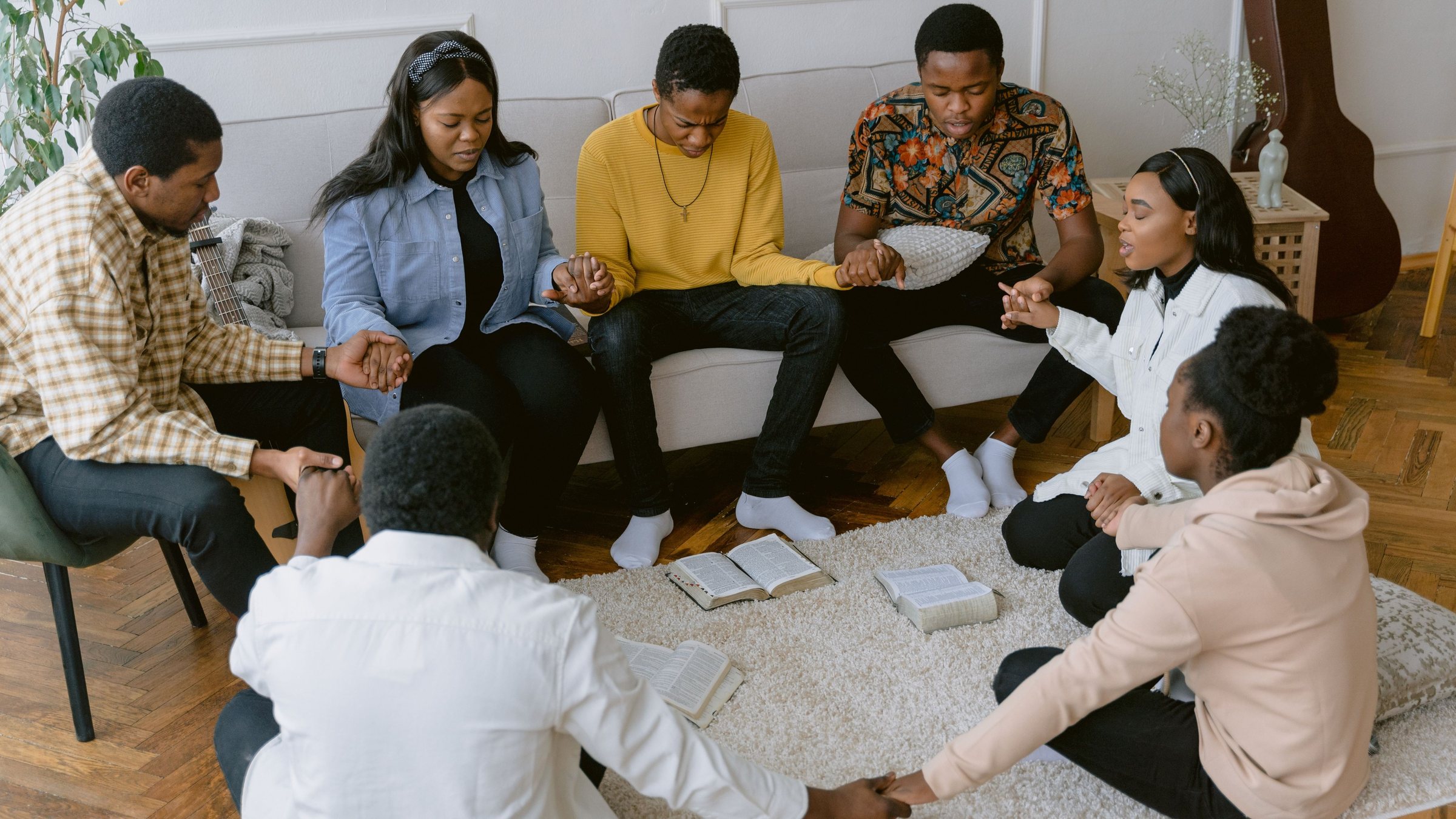 Students praying together in a circle, holding hands around open Bibles
